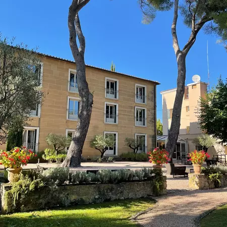 A tan stone building with trees and plants in front of it.