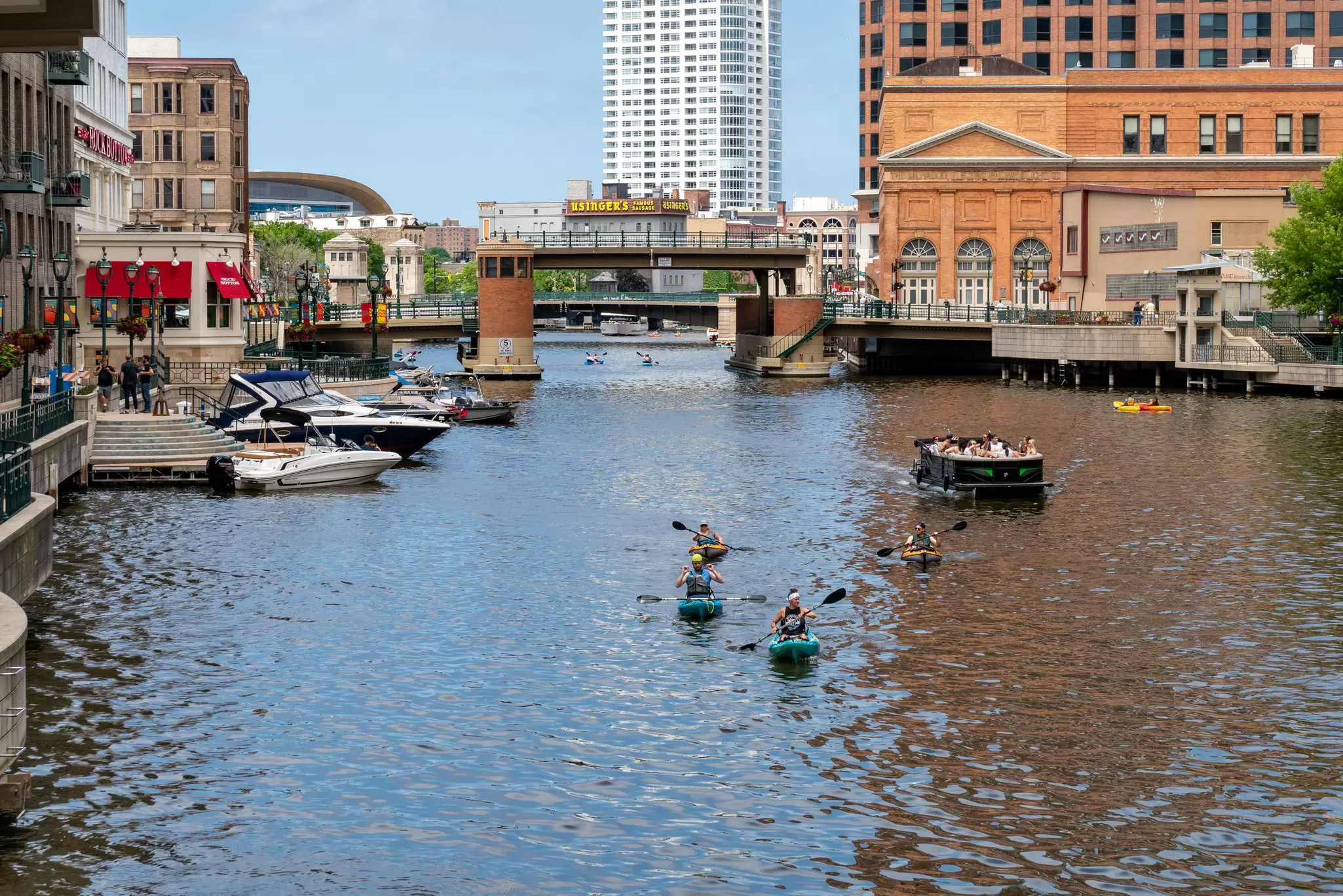 Unidentified individuals kayaking and boating on the Milwaukee River in downtown Milwaukee's Riverwalk.  
