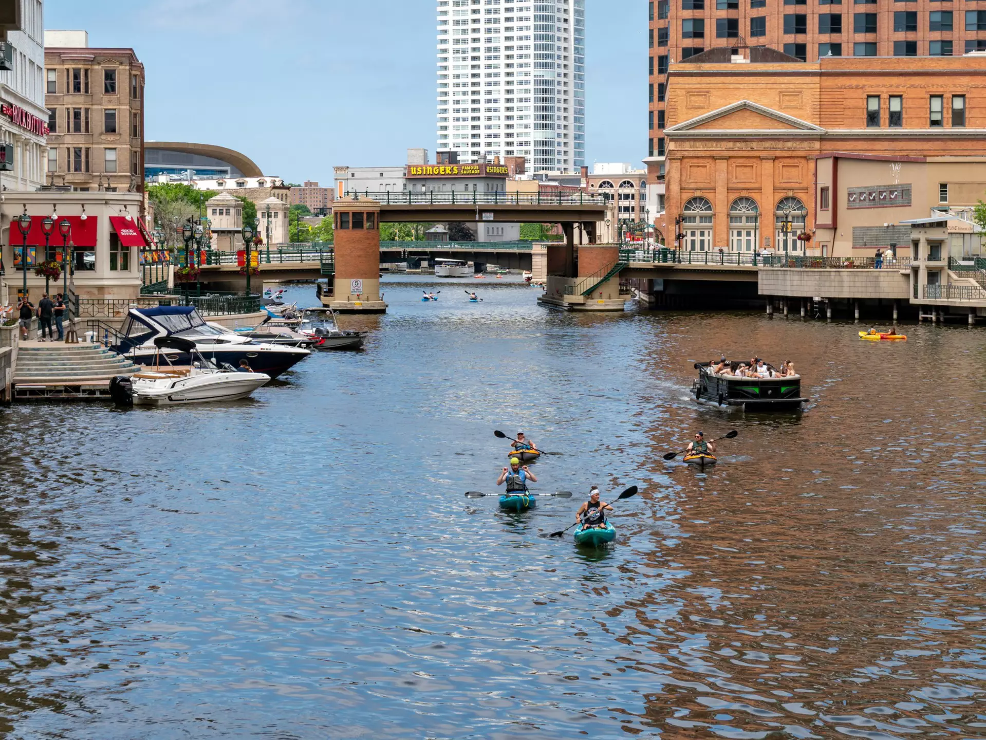 Unidentified individuals kayaking and boating on the Milwaukee River in downtown Milwaukee's Riverwalk.  