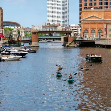 Unidentified individuals kayaking and boating on the Milwaukee River in downtown Milwaukee's Riverwalk.  