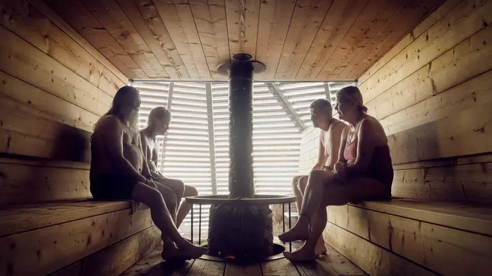 Four people sit in a wooden sauna in Helsinki with a pipe in the center.