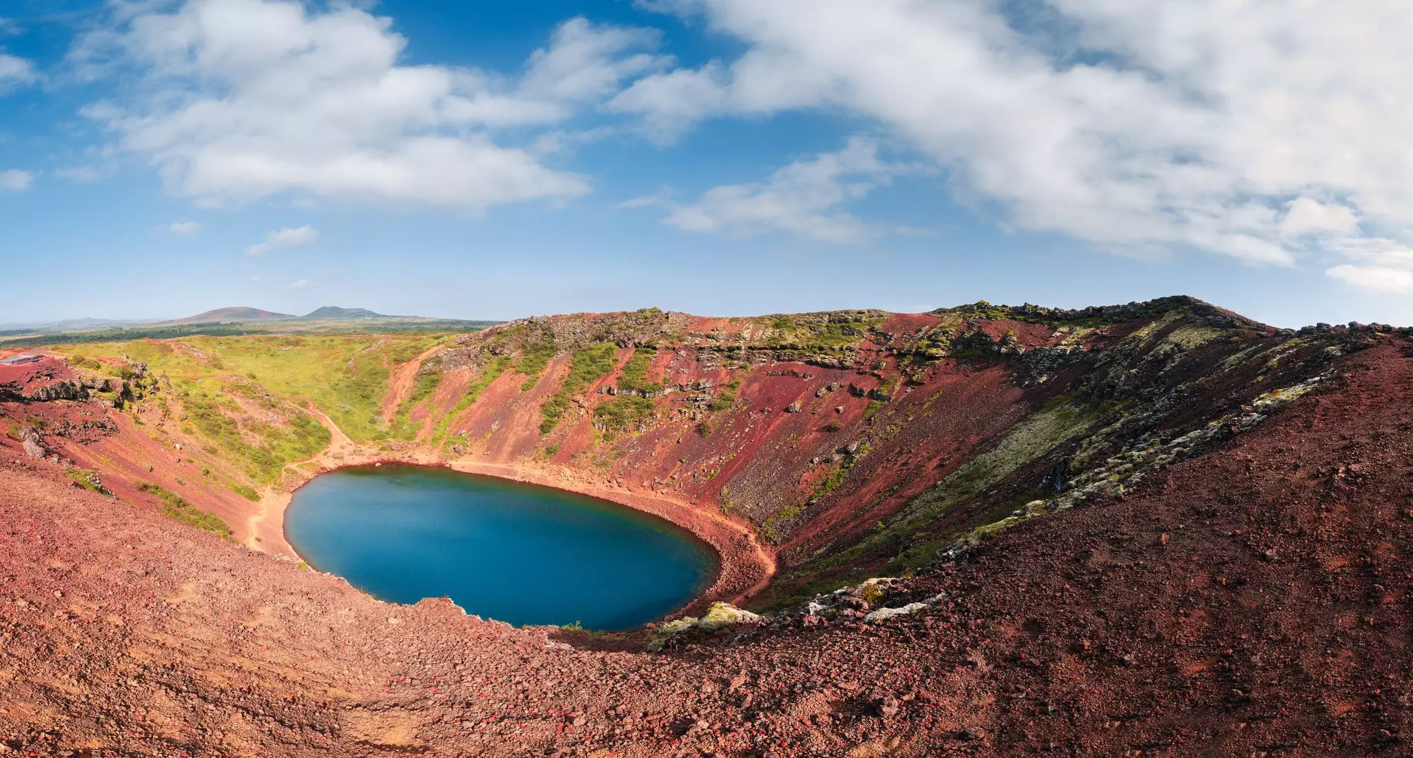 A vast volcanic crater lake bathed in sunlight. The rocks around it glow red.
