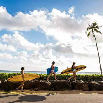 Pacific Islander surfers carry their boards to the water.