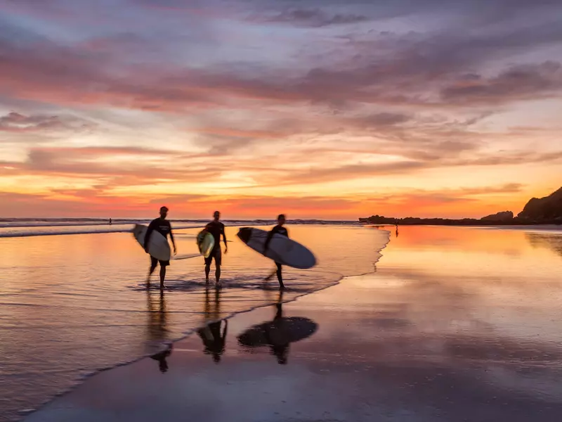 Surfers at sunset walking at Playa Guiones, Costa Rica