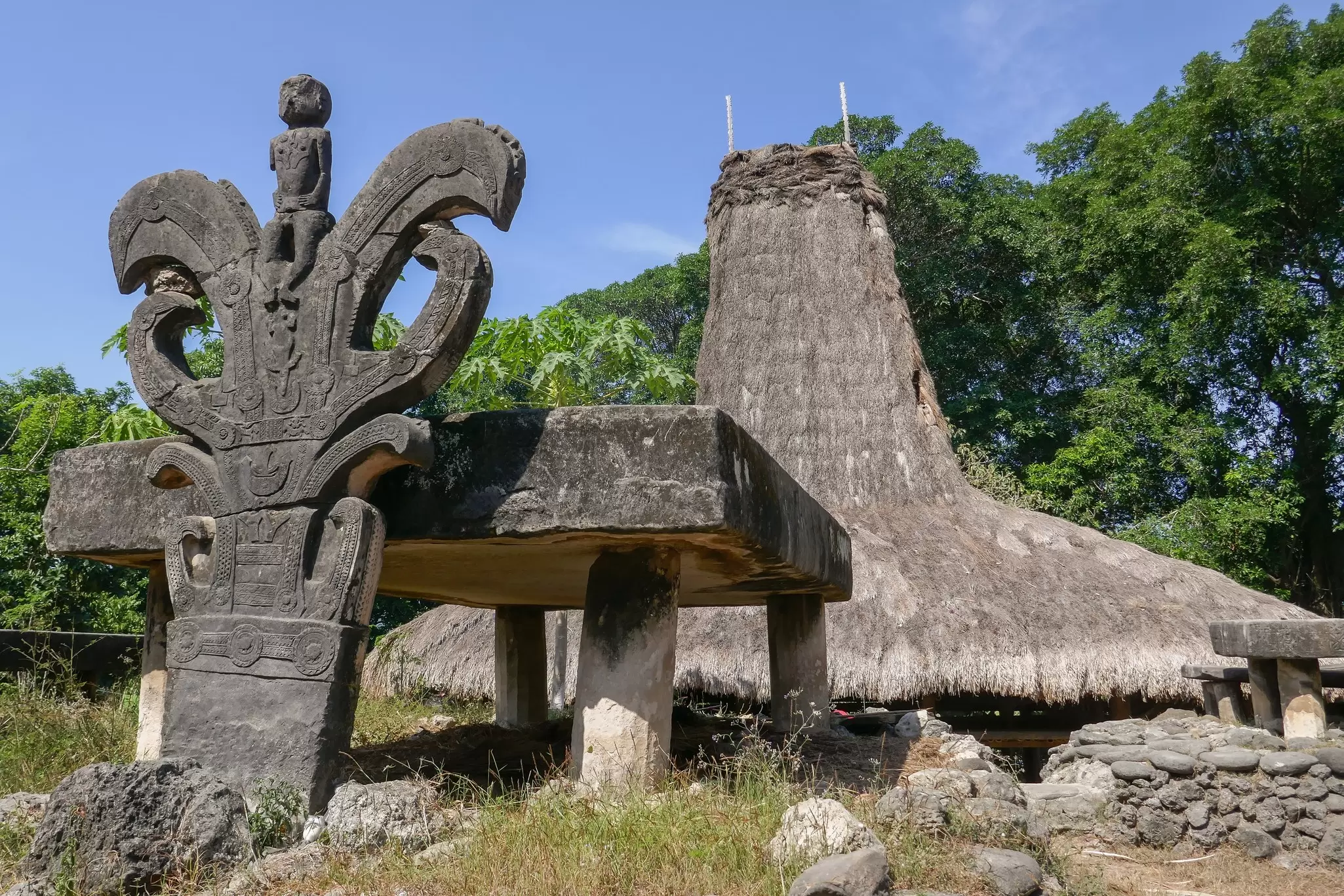 Carved, ancient megaliths stand before a traditional thatched structure, Watu Kajiwa megalithic tomb, Prai Goli village, Sumba, Nusa Tenggara, Indonesia