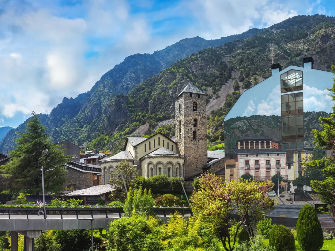 Sant Esteve church with its square stone bell tower and rounded apse beneath green mountains in Andorra la Vella