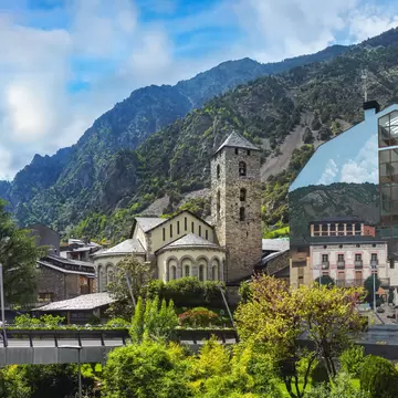 Sant Esteve church with its square stone bell tower and rounded apse beneath green mountains in Andorra la Vella