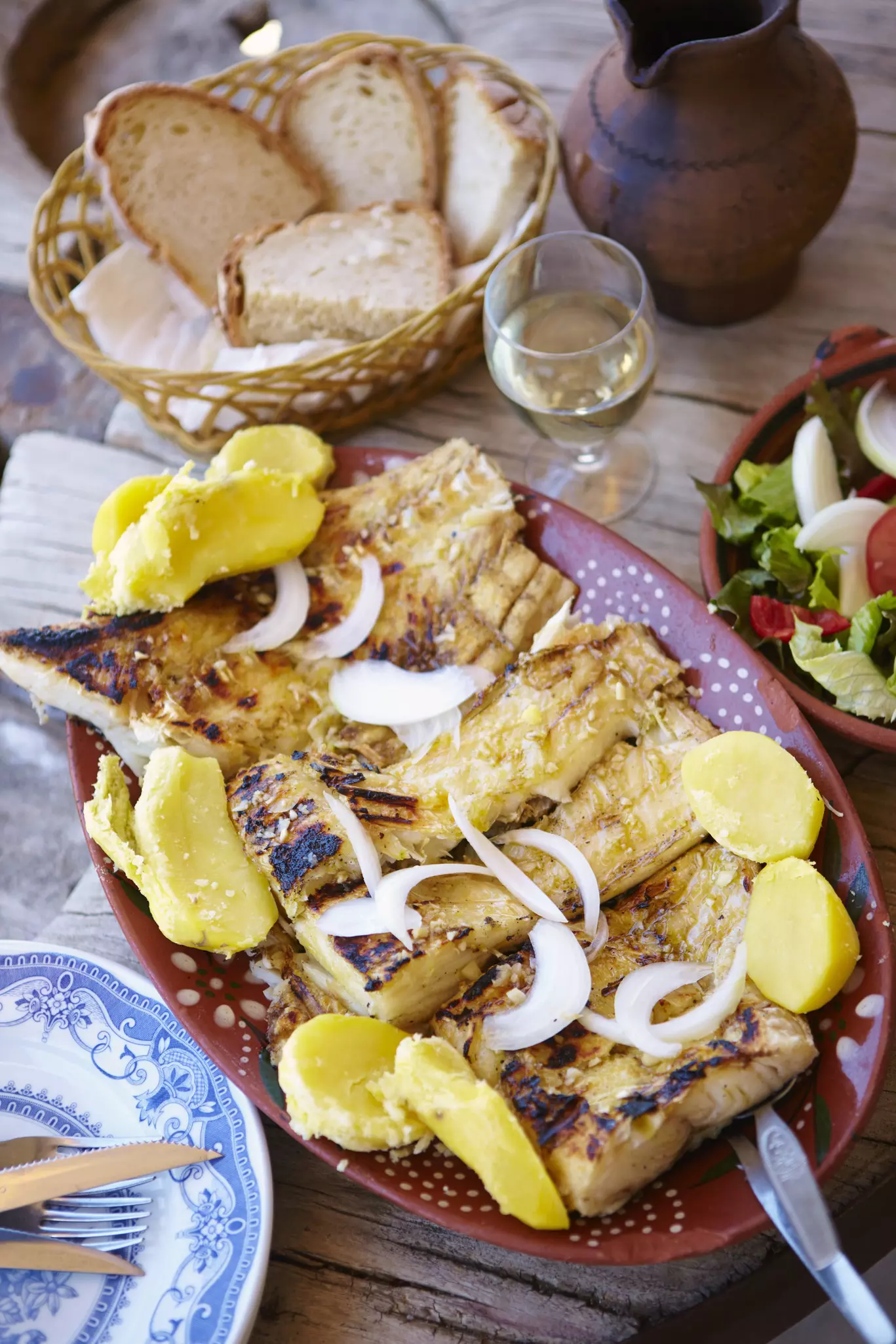 A dish of salted cod surrounded by potatoes near a basket of bread