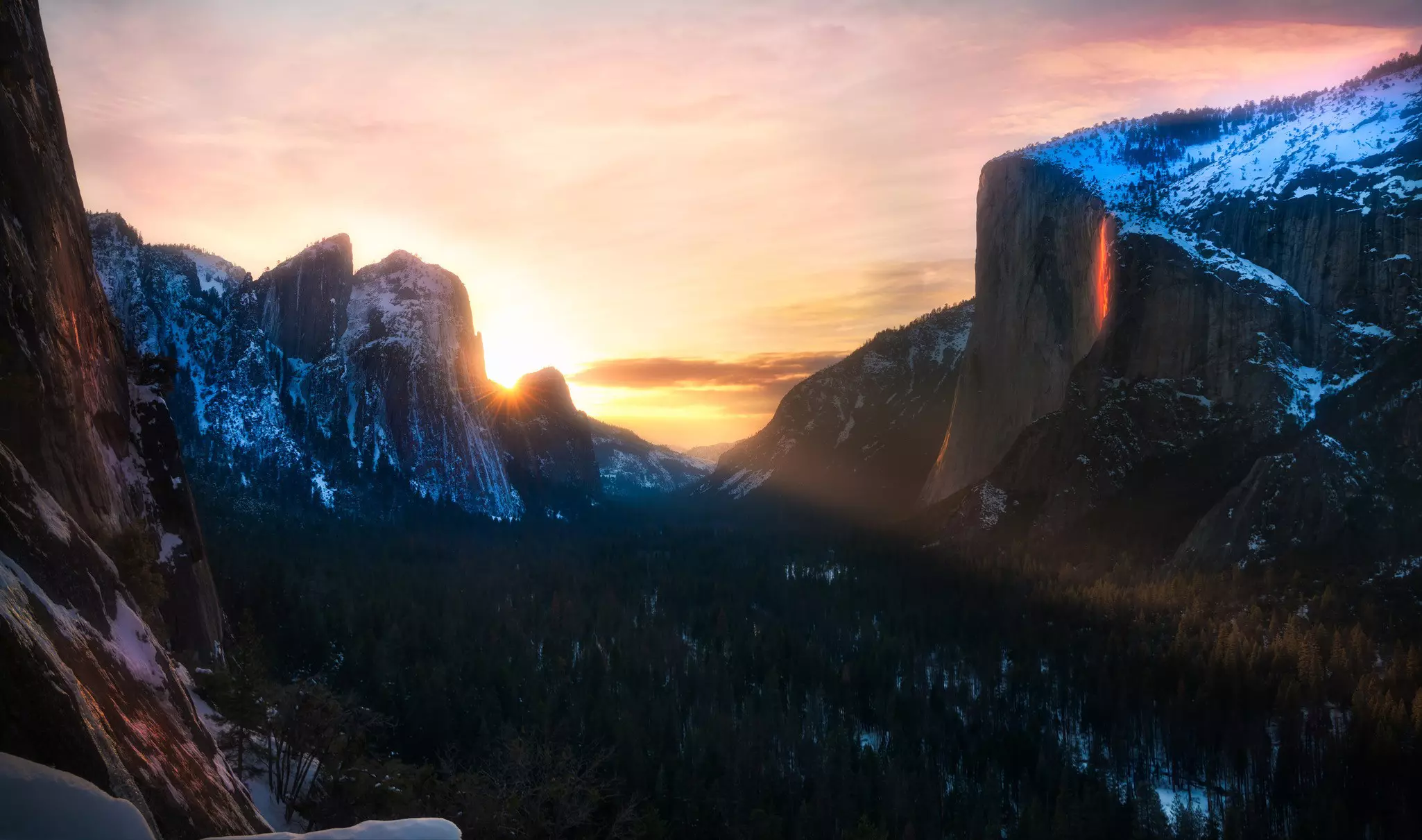 The sun sets behind a mountain range. A brightness that appears to be lava glows on a mountainside.