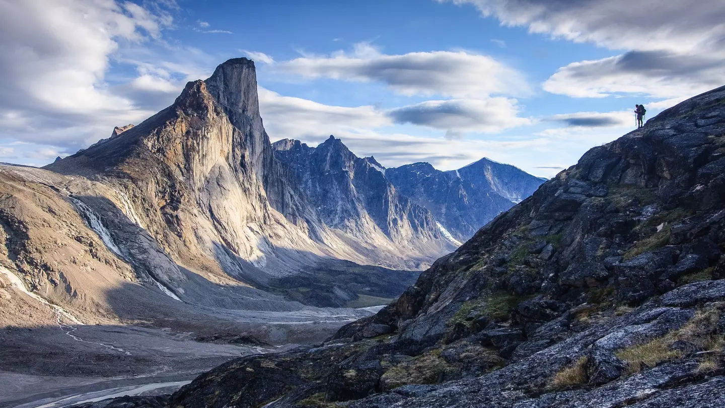 Silhouette of lone hiker on ridge looking across at Mount Thor in Akshayuk Pass, Nunavut, Canada.