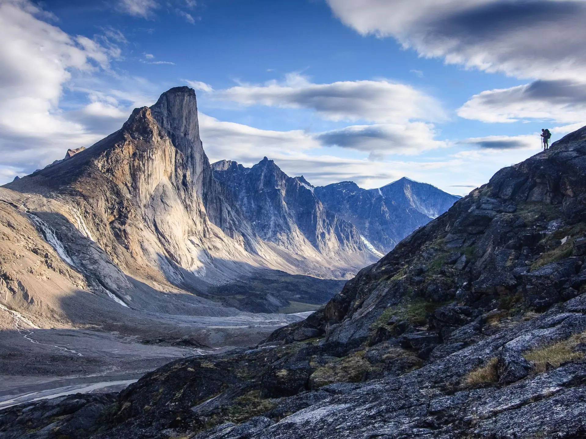 Silhouette of lone hiker on ridge looking across at Mount Thor in Akshayuk Pass, Nunavut, Canada.