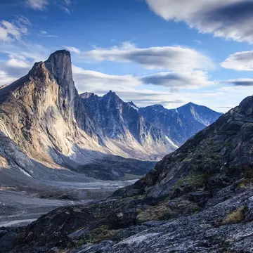 Silhouette of lone hiker on ridge looking across at Mount Thor in Akshayuk Pass, Nunavut, Canada.