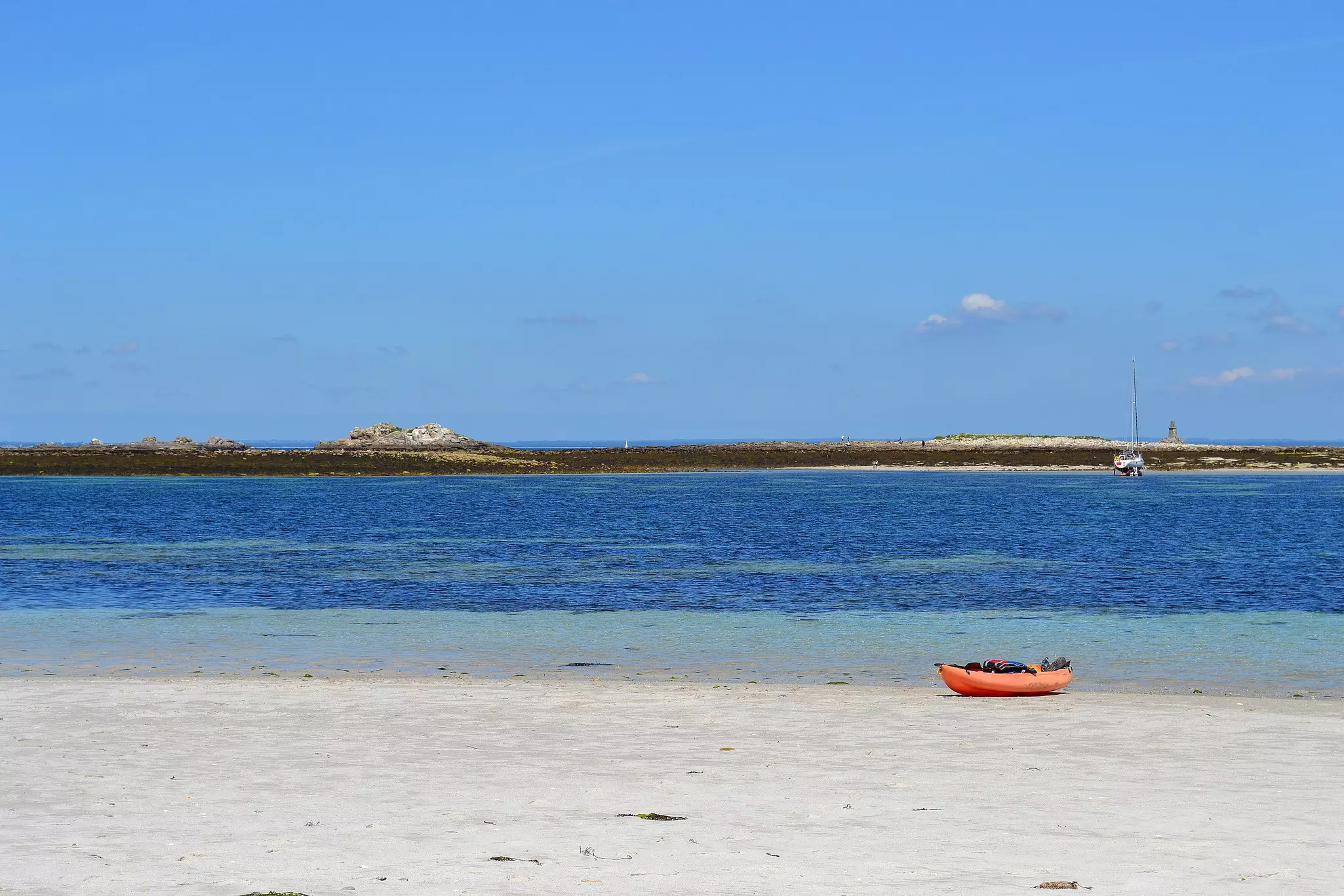 A single red kayak on an empty beach by blue water.