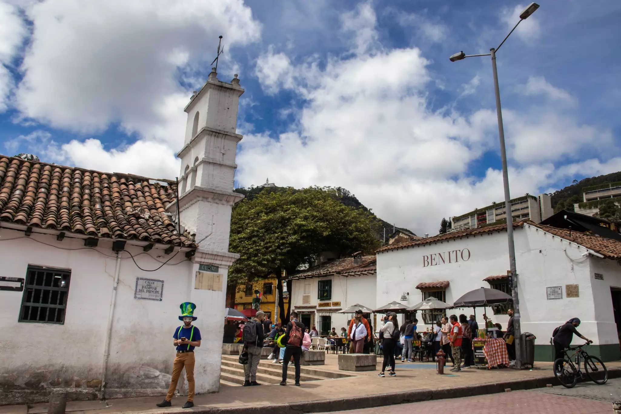 People stand in a small square lined with historic white-painted buildings with tiled roofs.