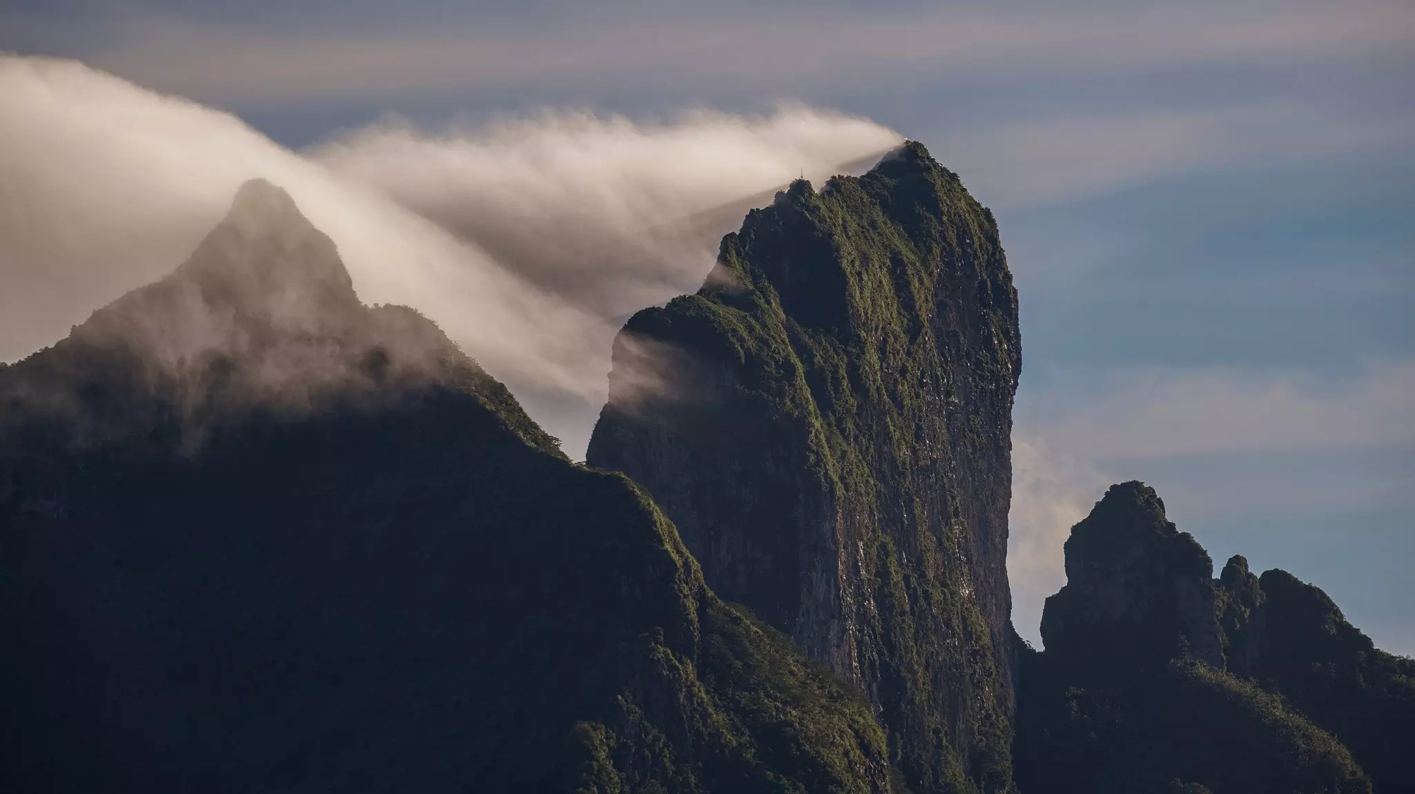 A close-up shot of misty clouds hugging rocky, spiky peaks of a mountain on a tropical island