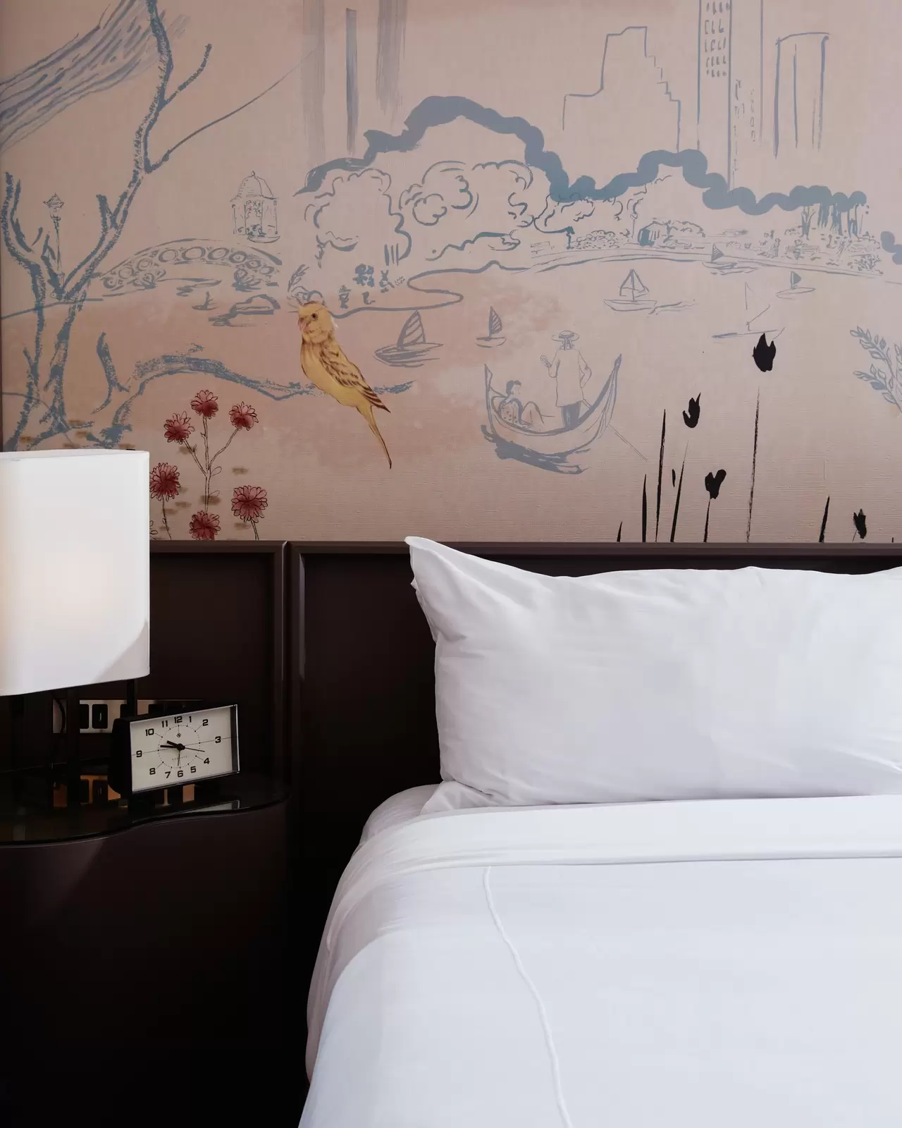 A white bed in a hotel room with patterned wallpaper behind the headboard.