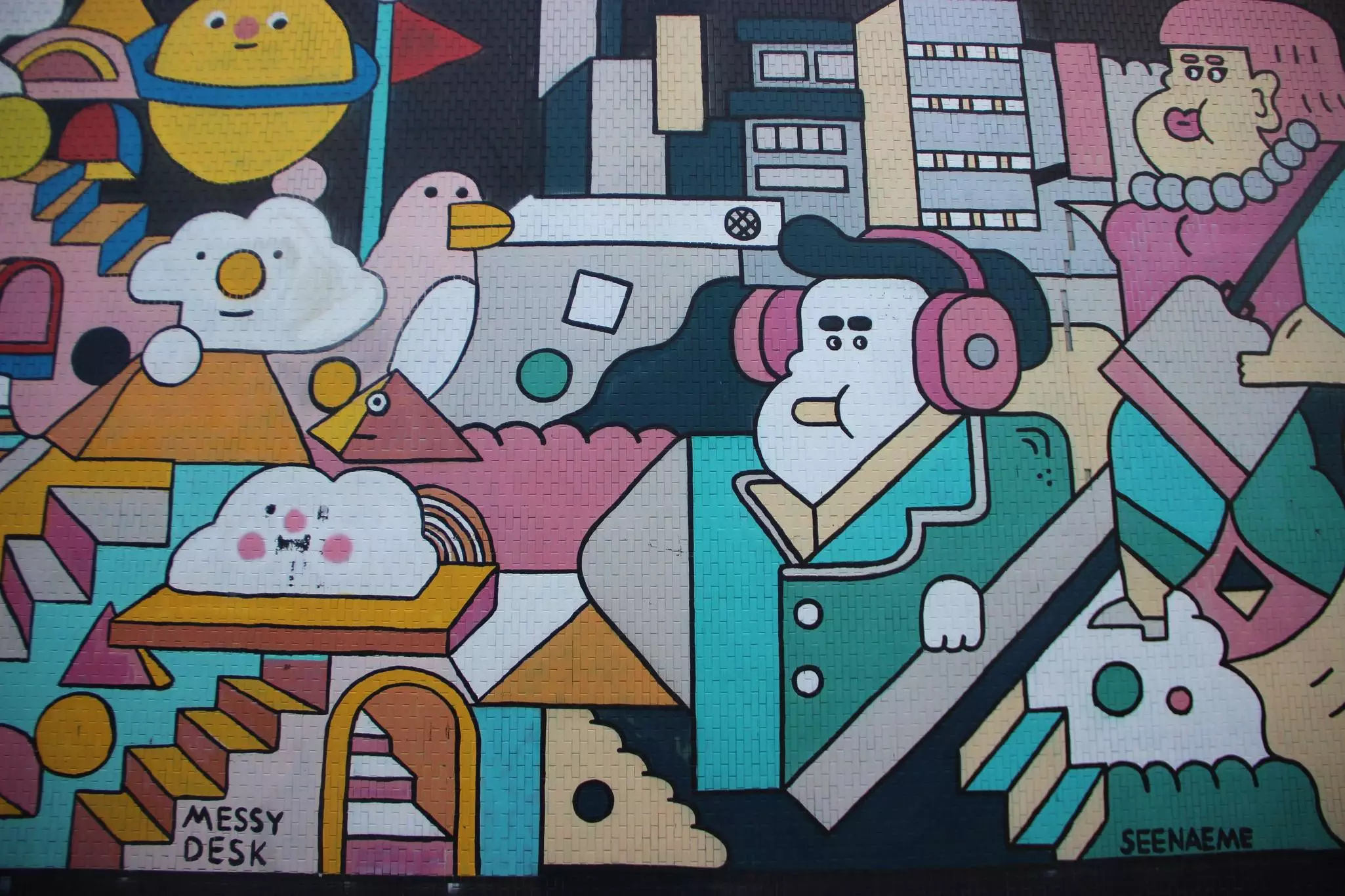 Image of bright painted street art on brick building of cartoon-like characters, including people, birds, and clouds with faces.