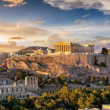 The Acropolis of Athens, Greece, crowned by the columns of the Parthenon temple, on top of a hill during a summer sunset.