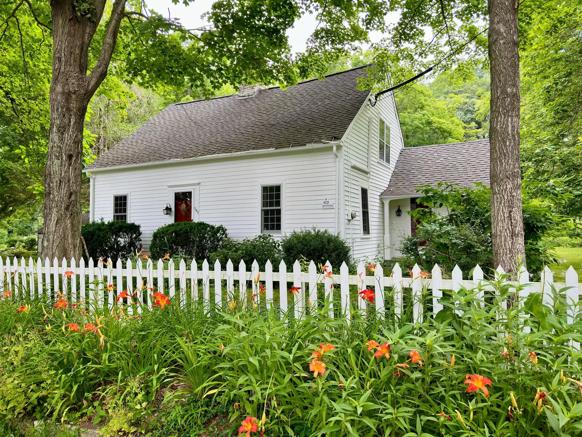 Guilford, Connecticut, USA - July 17, 2024:  Vintage, white house surrounded by nature.  Wooden fence in foreground with orange daylily flowers.  Summer, residential scene.   , License Type: media, Download Time: 2024-09-09T04:37:34.000Z, User: Norma.PrauseBrewer_LonelyPlanet, Editorial: true, purchase_order: 56530, job: Global Publishing WIP, client: New England 11, other: Norma Brewer