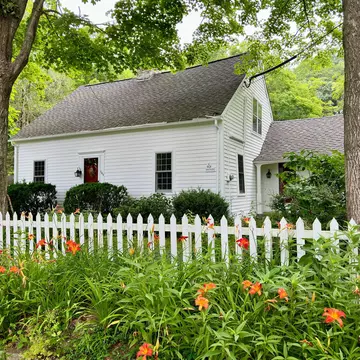 Guilford, Connecticut, USA - July 17, 2024:  Vintage, white house surrounded by nature.  Wooden fence in foreground with orange daylily flowers.  Summer, residential scene.   , License Type: media, Download Time: 2024-09-09T04:37:34.000Z, User: Norma.PrauseBrewer_LonelyPlanet, Editorial: true, purchase_order: 56530, job: Global Publishing WIP, client: New England 11, other: Norma Brewer