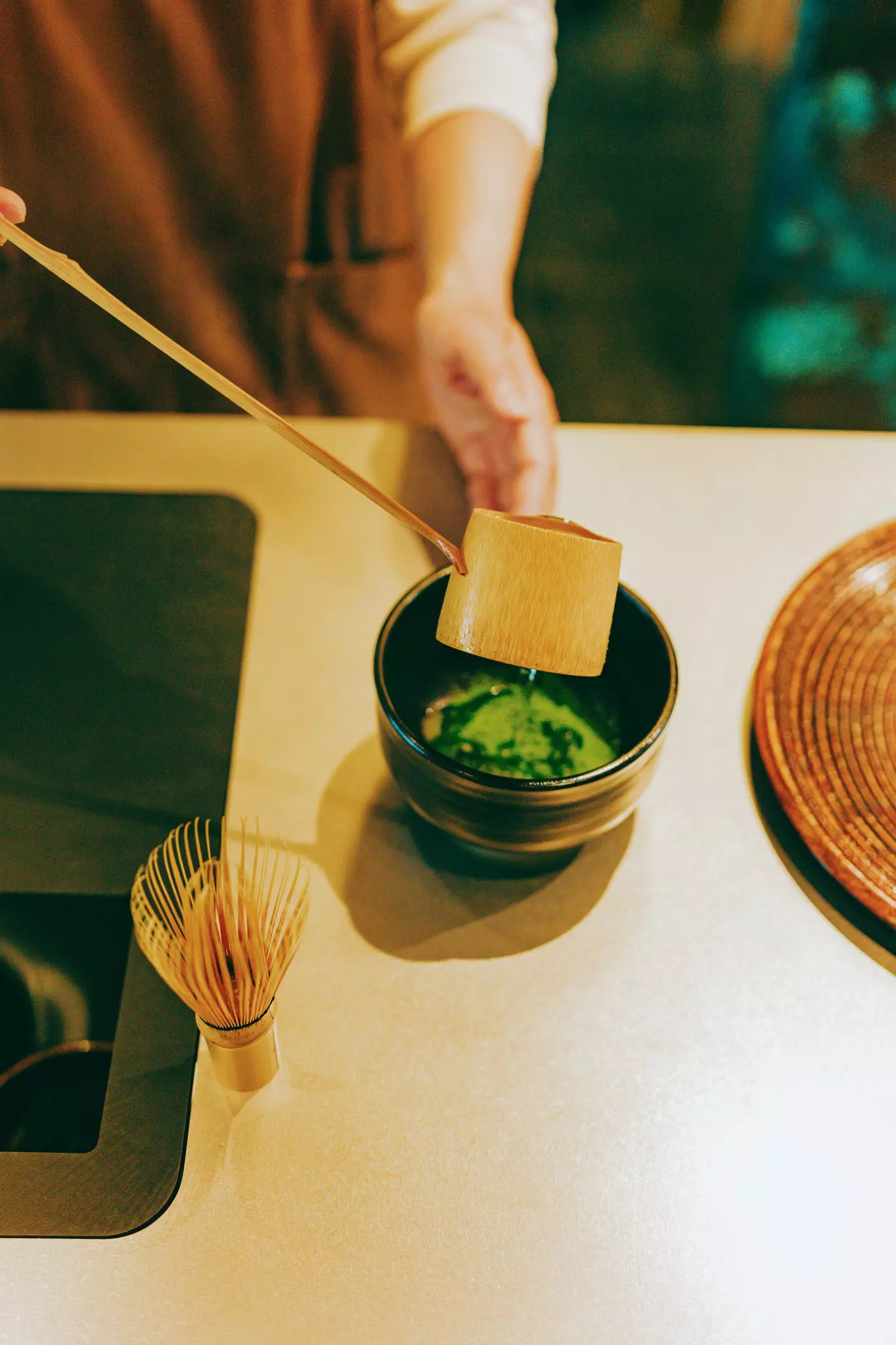 A ladle of hot water being poured over green tea in a bowl
