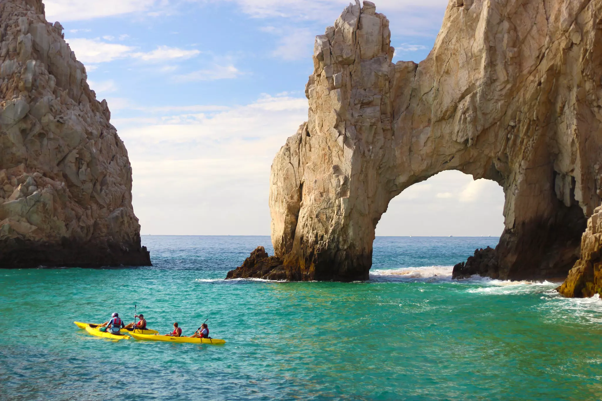 People enjoying a kayak ride in yellow kayak wearing life vests along the impressive landmark stone arc on beautiful turquoise waters at Cabo San Lucas on nice sunny sky  License Type: media  Download Time: 2022-03-23T22:14:12.000Z  User: bhealy950  Is Editorial: No  purchase_order: