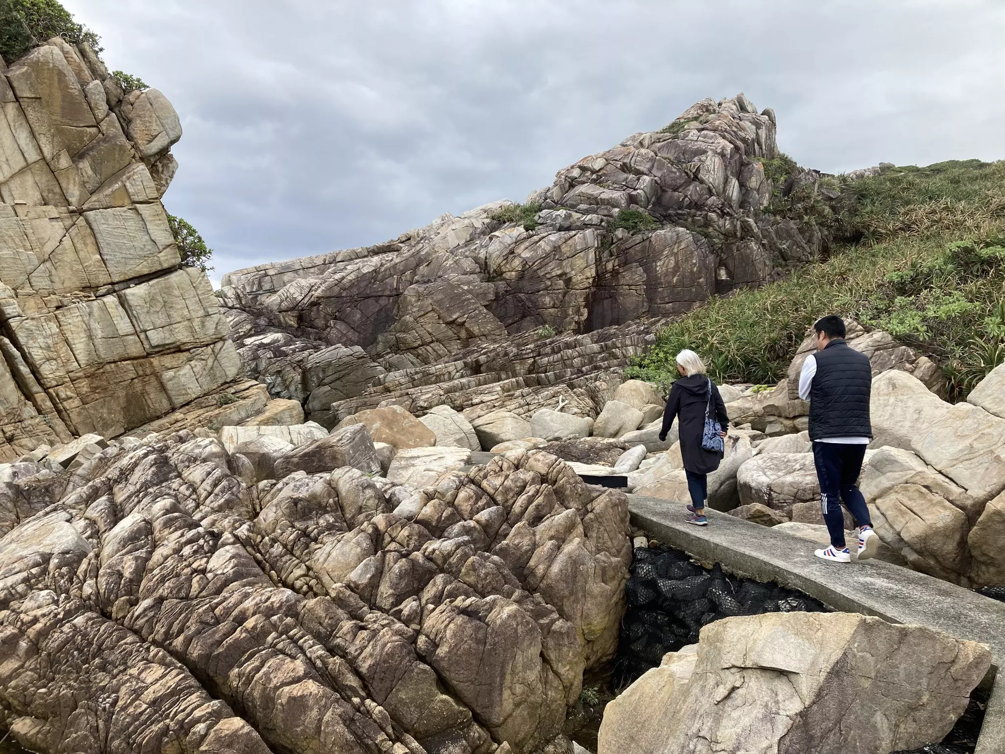 Two people walk along a rock bridge among vast boulders.