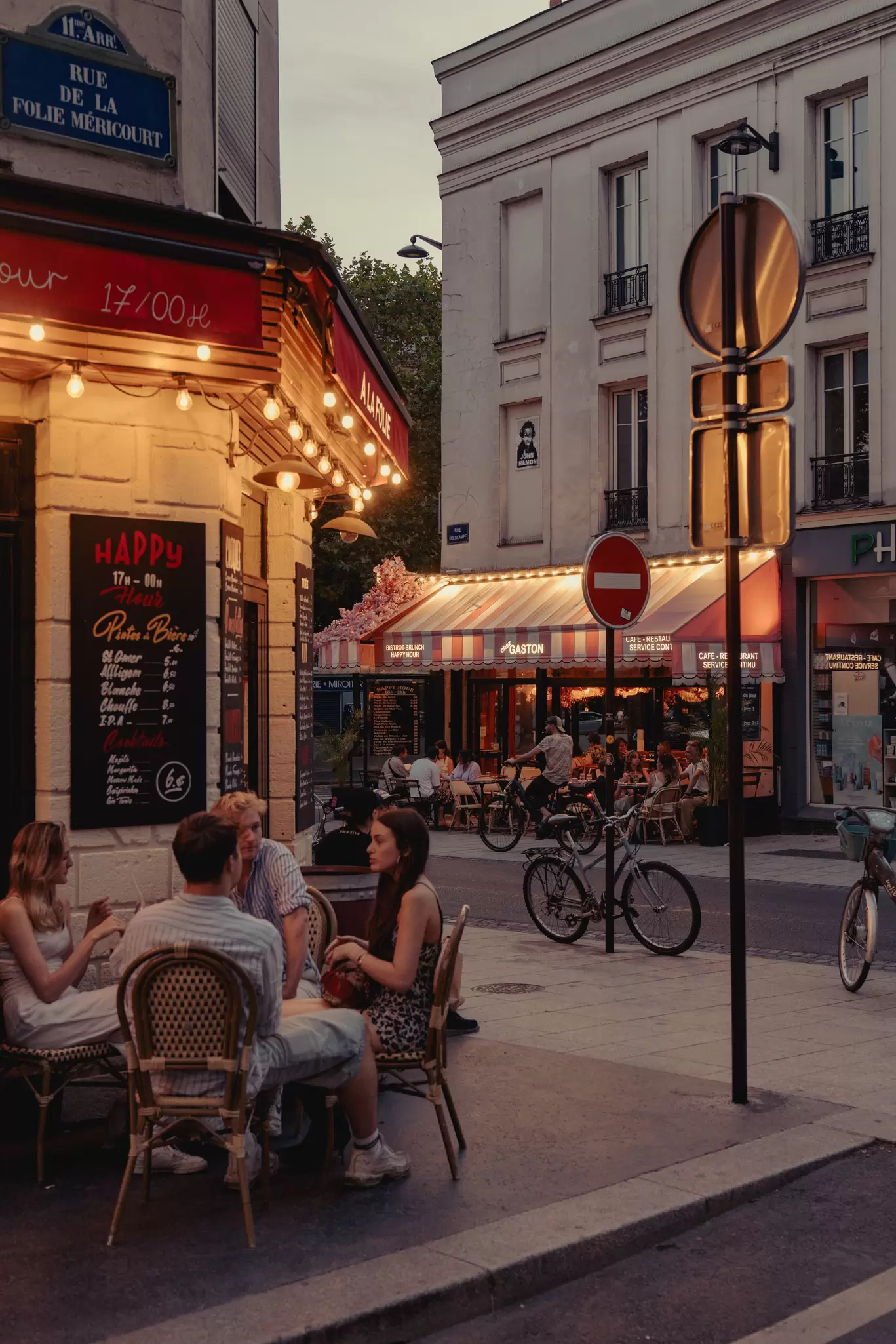 People sitting at a sidewalk cafe in early evening.