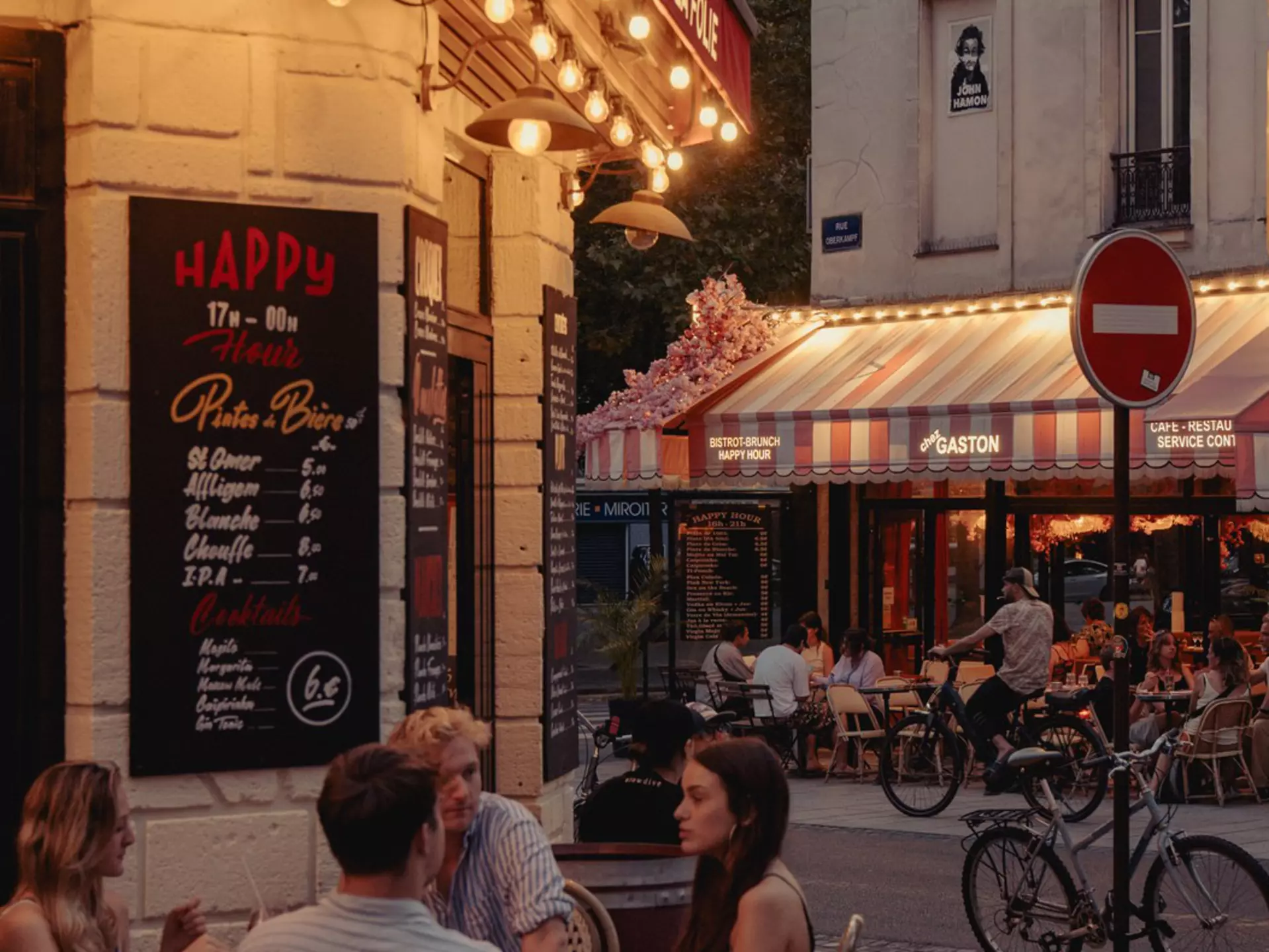 People sitting at a sidewalk cafe in early evening.
