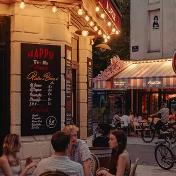 People sitting at a sidewalk cafe in early evening.