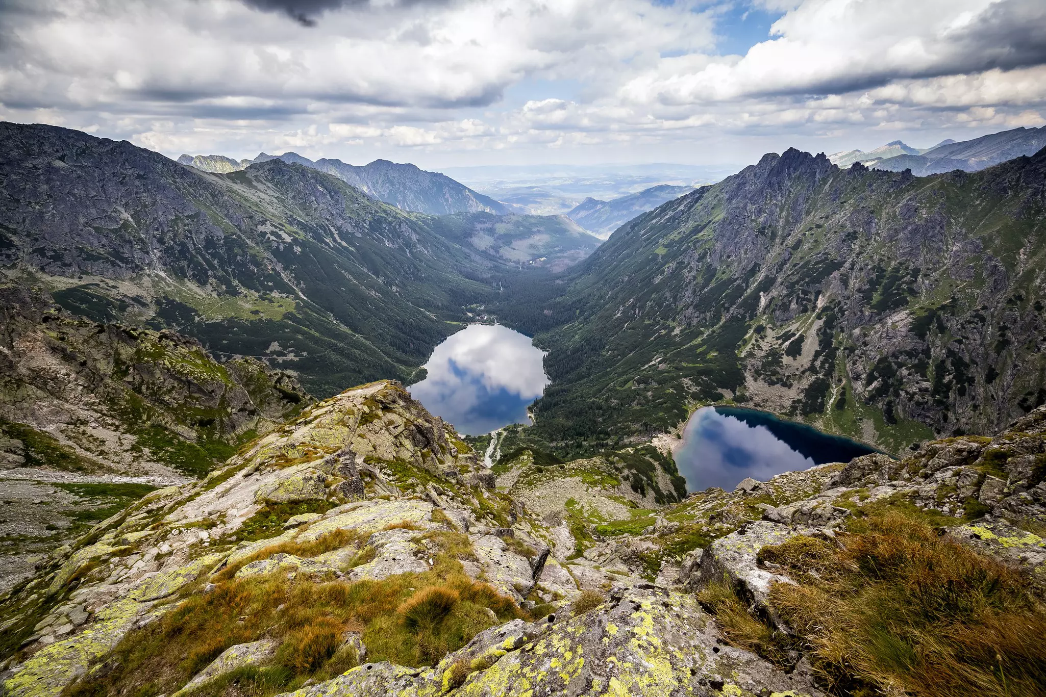 Two clear pools in a mountain valley; clouds are reflected on the water's surface.