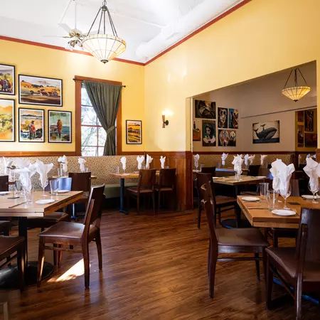 Dining room with tables set for four including wine glasses with white napkins.