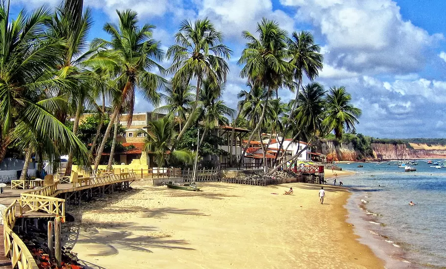 Praia da Pipa, Brazil, golden beach under leaning coconut palms with a wooden boardwalk and red-ochre cliffs
