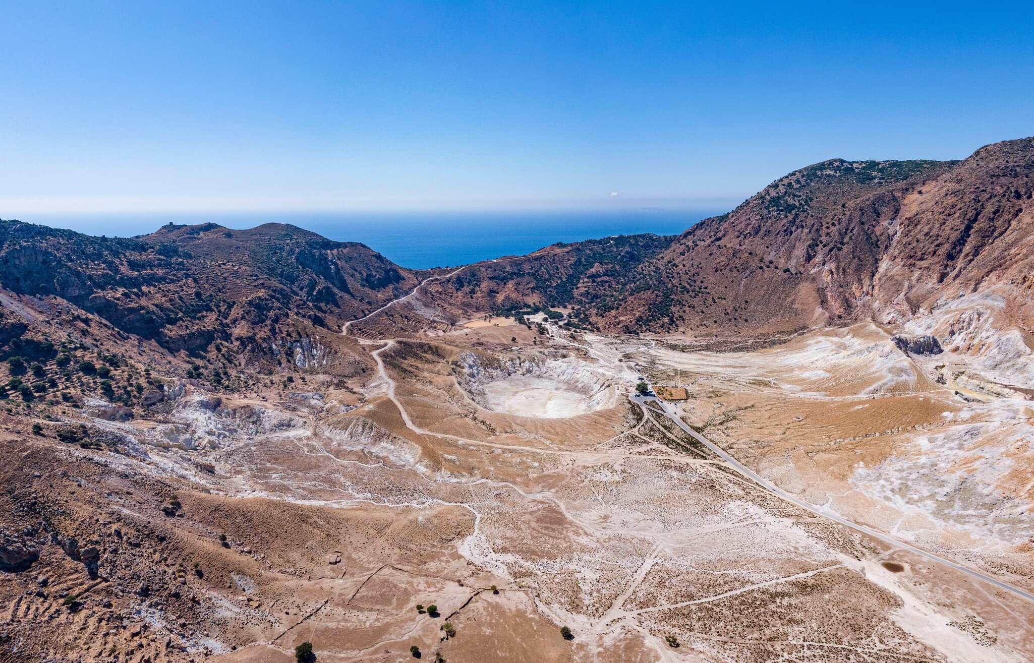 Aerial of the Stefanos volcano crater on Nisyros Island, with the Aegean sea in the background.