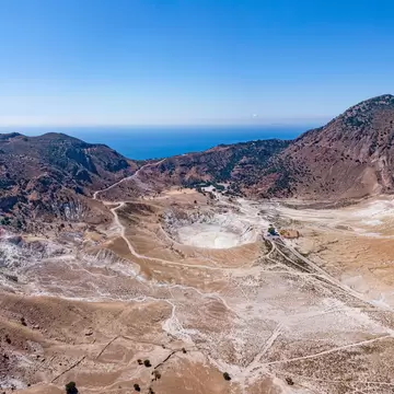 Aerial of the Stefanos volcano crater on Nisyros Island, with the Aegean sea in the background.