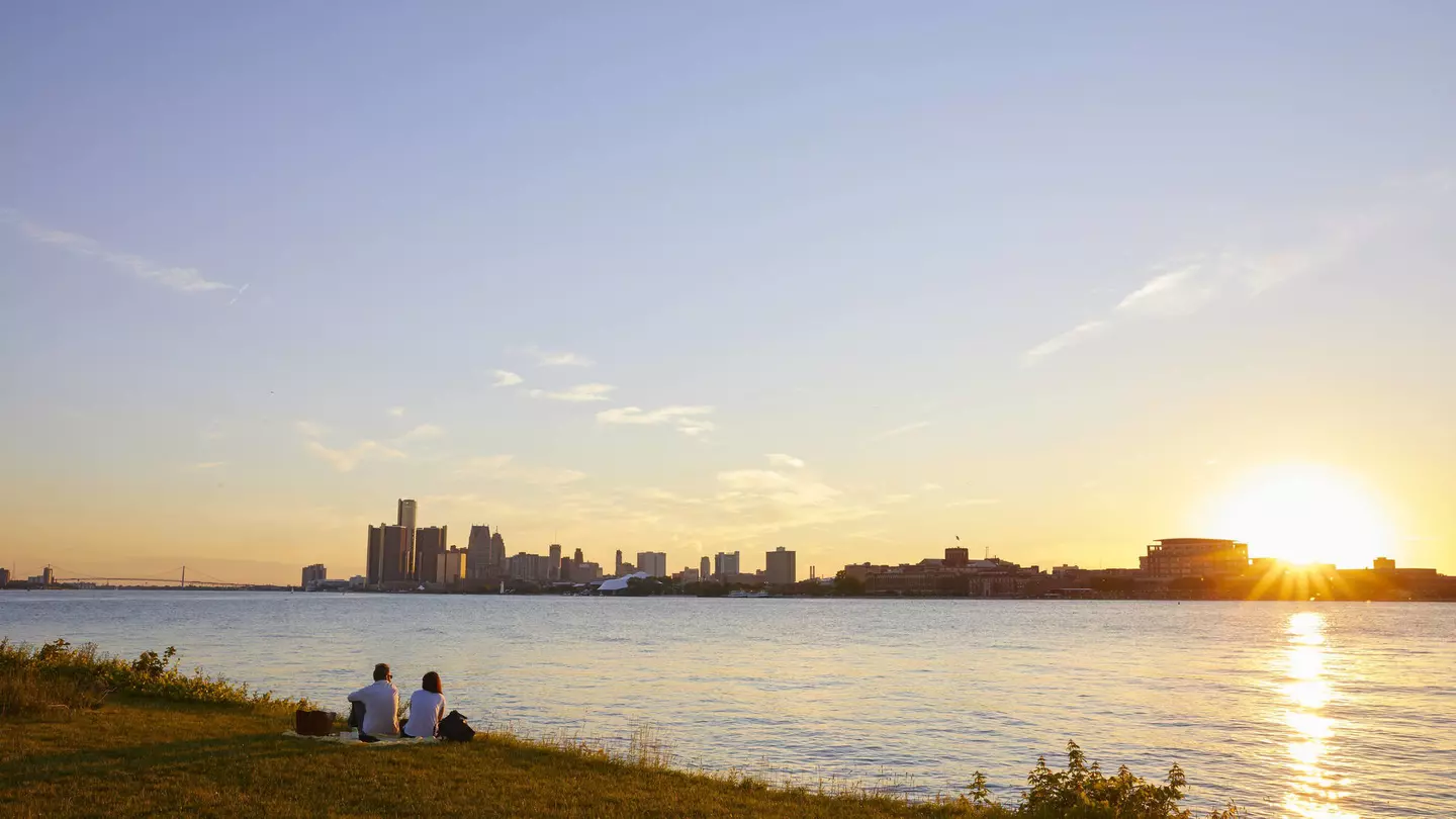 Two people watch the sunset from Belle Isle with the skyline of Detroit in the background