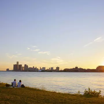 Two people watch the sunset from Belle Isle with the skyline of Detroit in the background