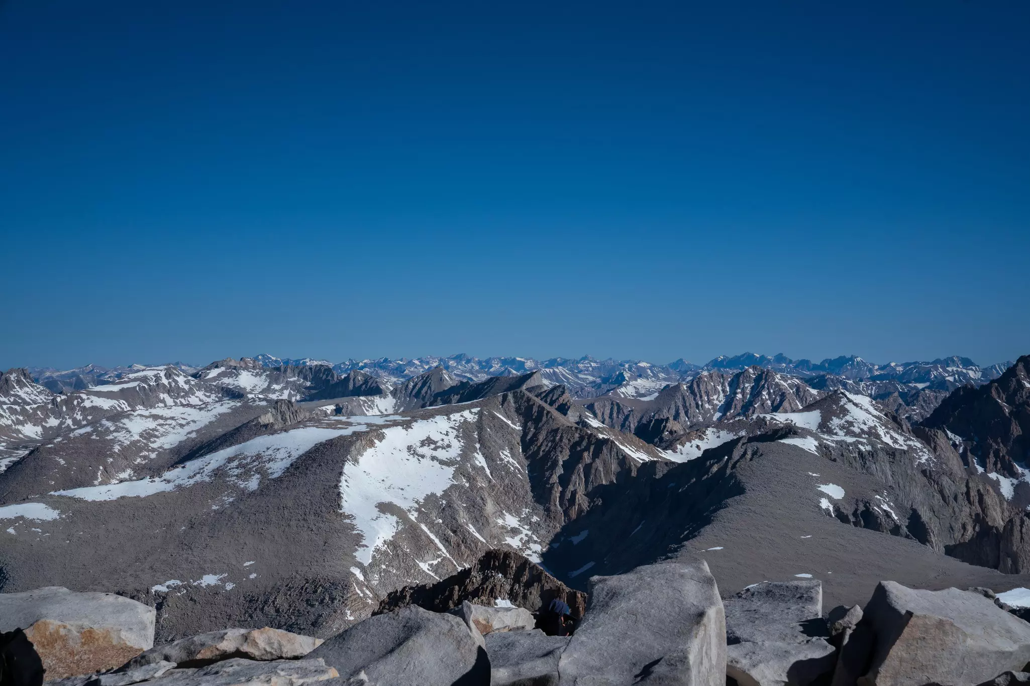 A mountain range stretches into the distance, with snow over escarpments and a blue sky above.