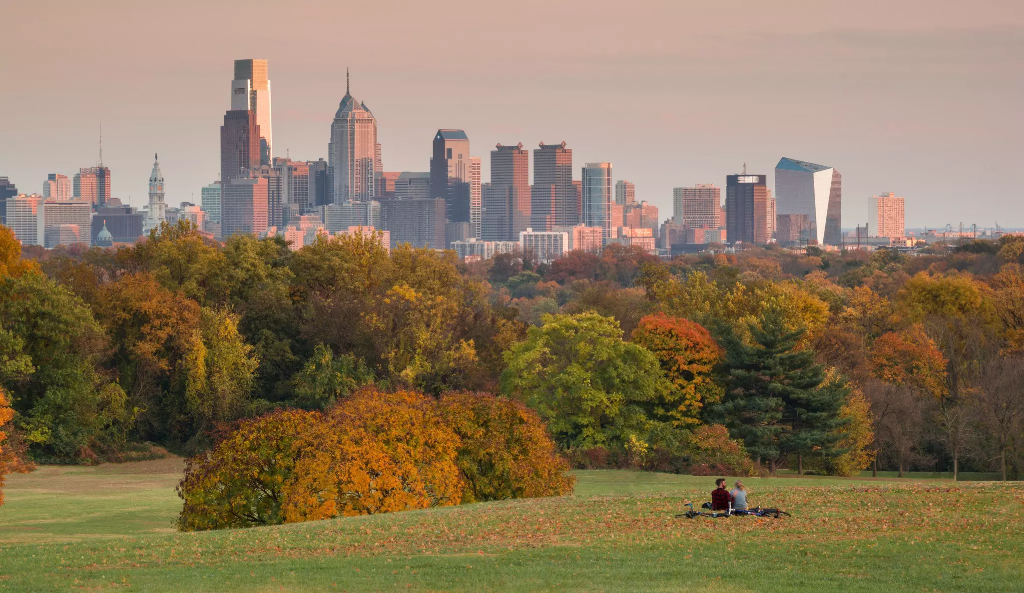 A couple with bicycles sit on the grass of Belmont Plateau in Fairmount Park during an autumn sunset.