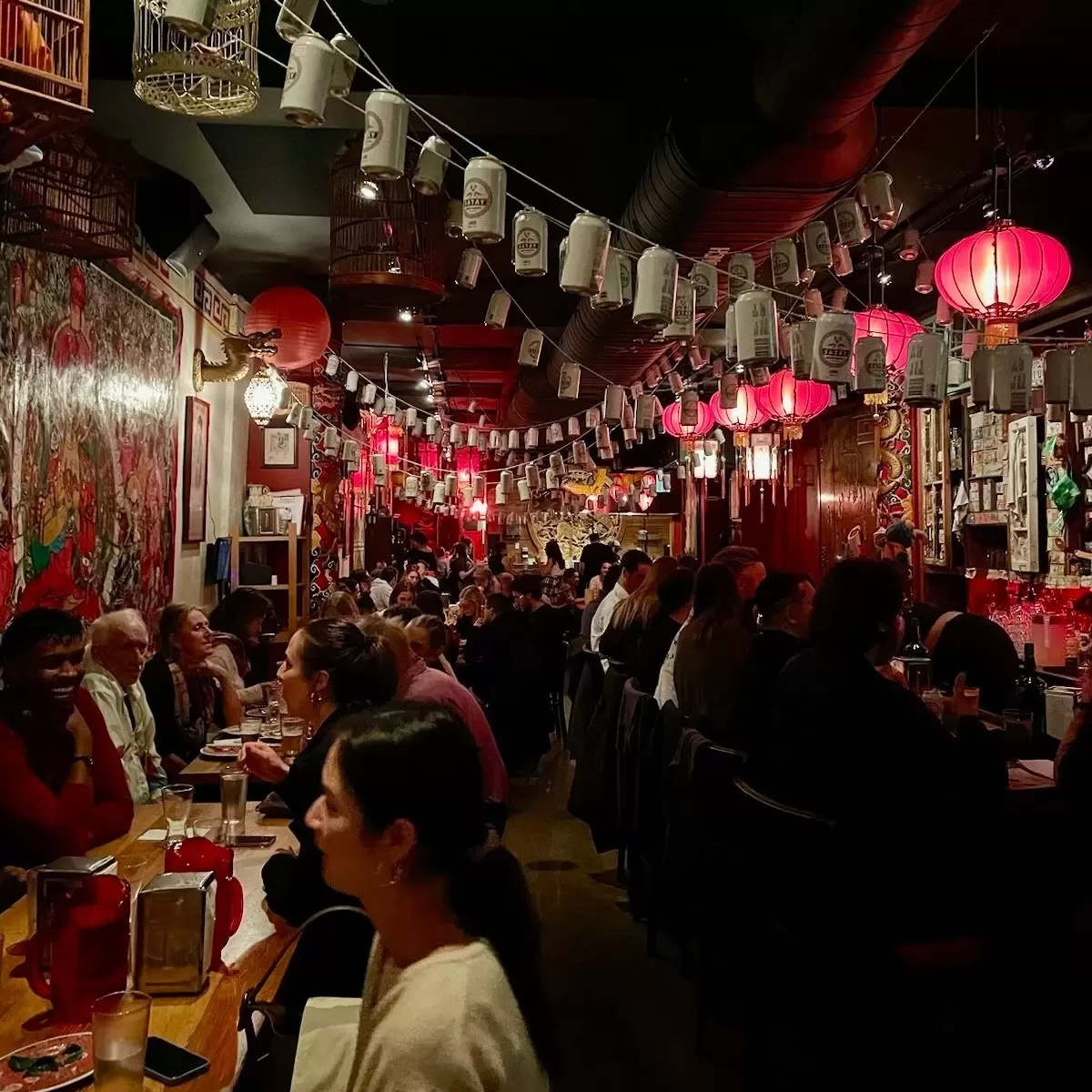 People sit at tables in a restaurant dining room hung with strings of lights and paper lanterns, Satay Brothers, Montréal