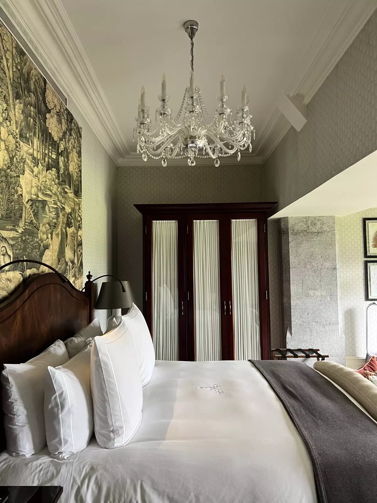 A king-sized bed in a hotel room with a glass chandelier hanging above it.