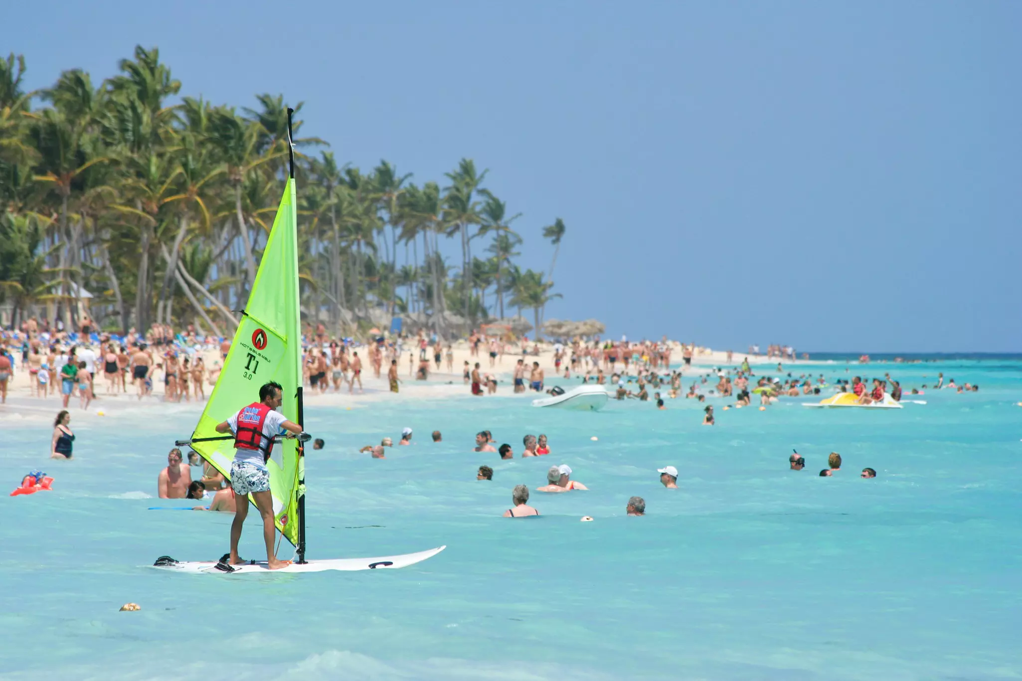 A windsurfer heads out on the ocean just offshore. Many people are in the sea