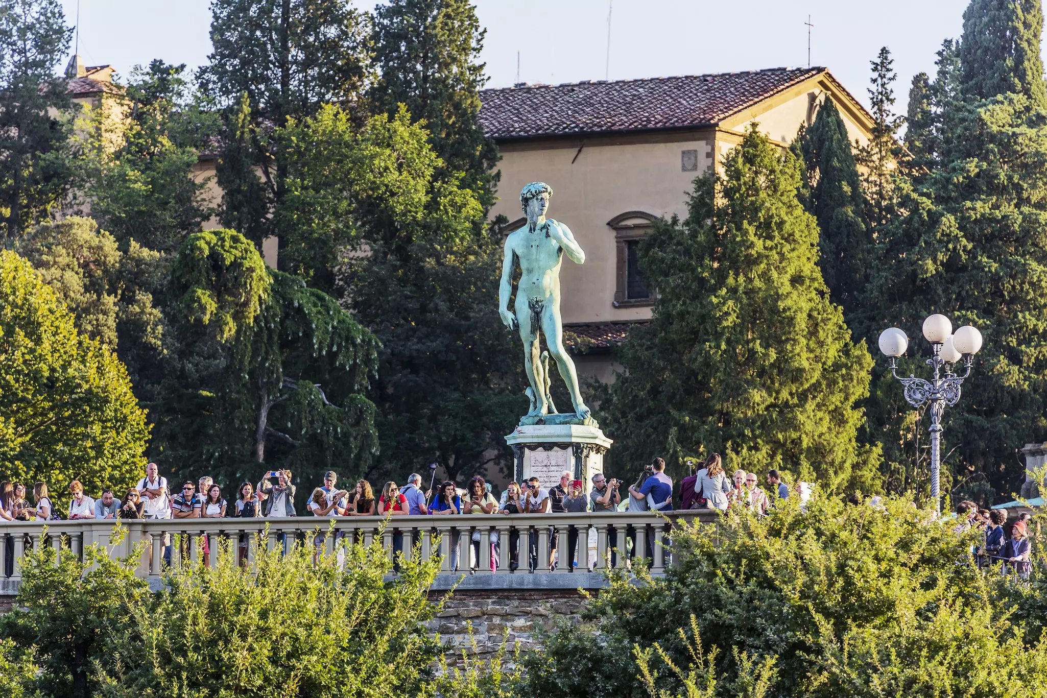 People at a viewpoint on a sunny day. Behind them stands a statue of a naked man.