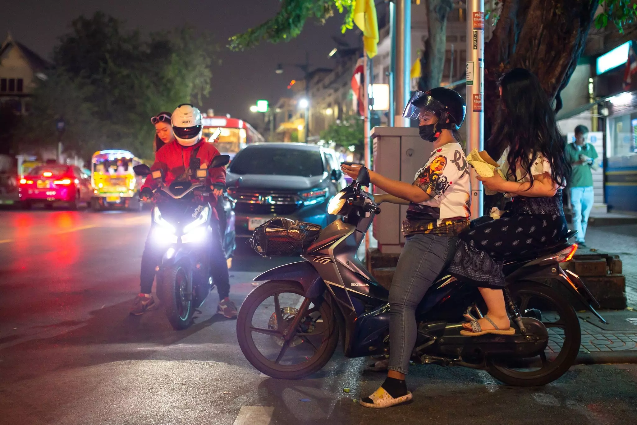 A woman and man ride a motorcycle taxi on a city street at night.