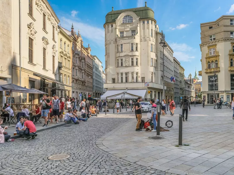 Young women and men drinking and chatting on a plaza on a sunny evening.