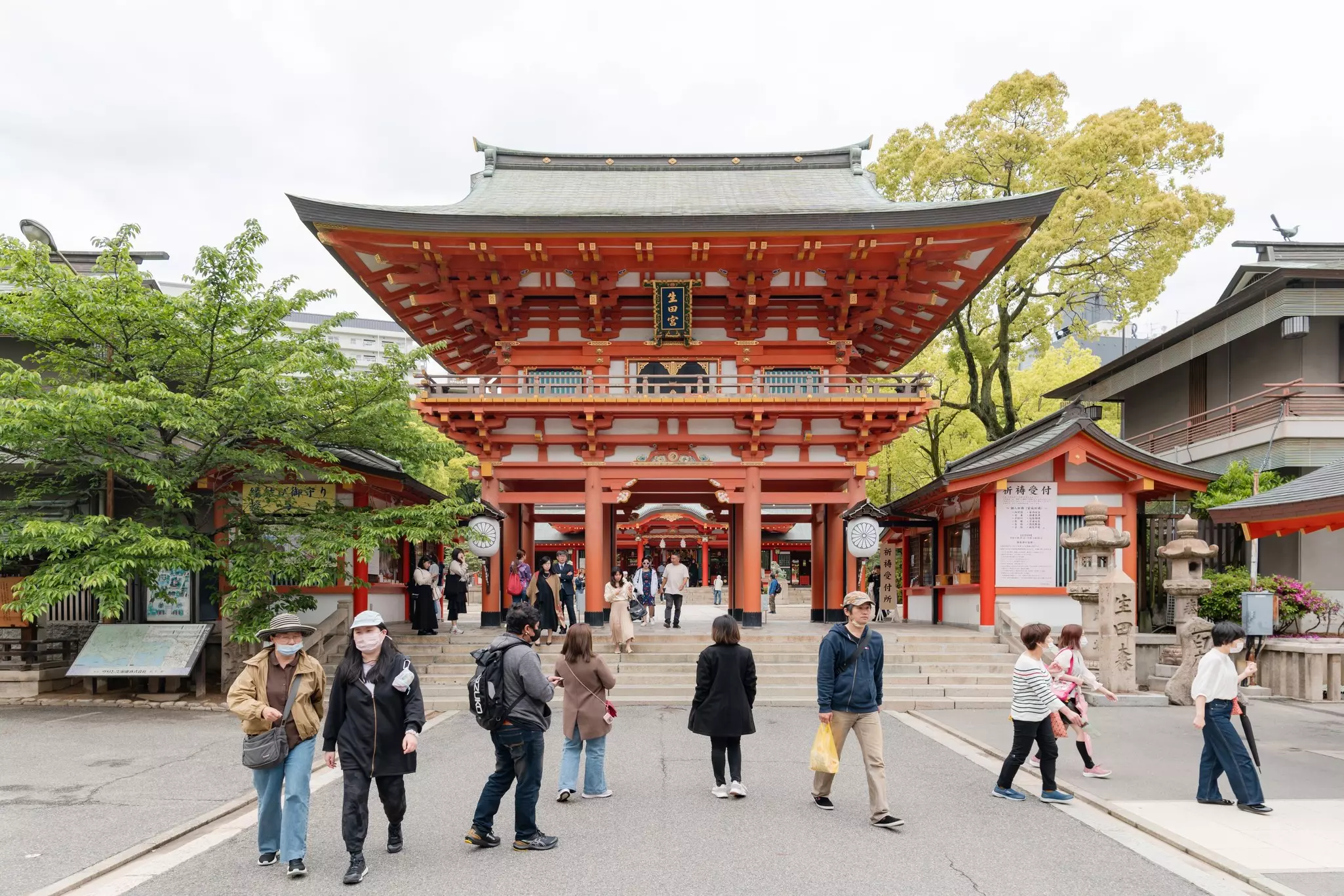 People walk in front of a large red gateway to a shrine in Kobe