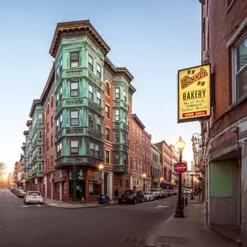 A charming five-storey heritage building painted green on a street corner in Little Italy, Boston