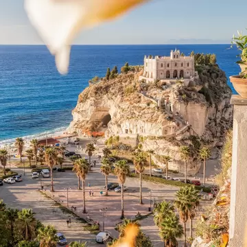 Santa Maria dell'Isola sanctuary on a rock above the beach in Tropea, Calabria, Italy, seen past blurred flowers
