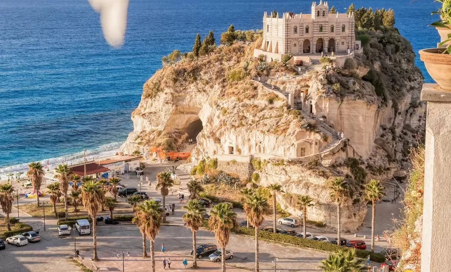 Santa Maria dell'Isola sanctuary on a rock above the beach in Tropea, Calabria, Italy, seen past blurred flowers