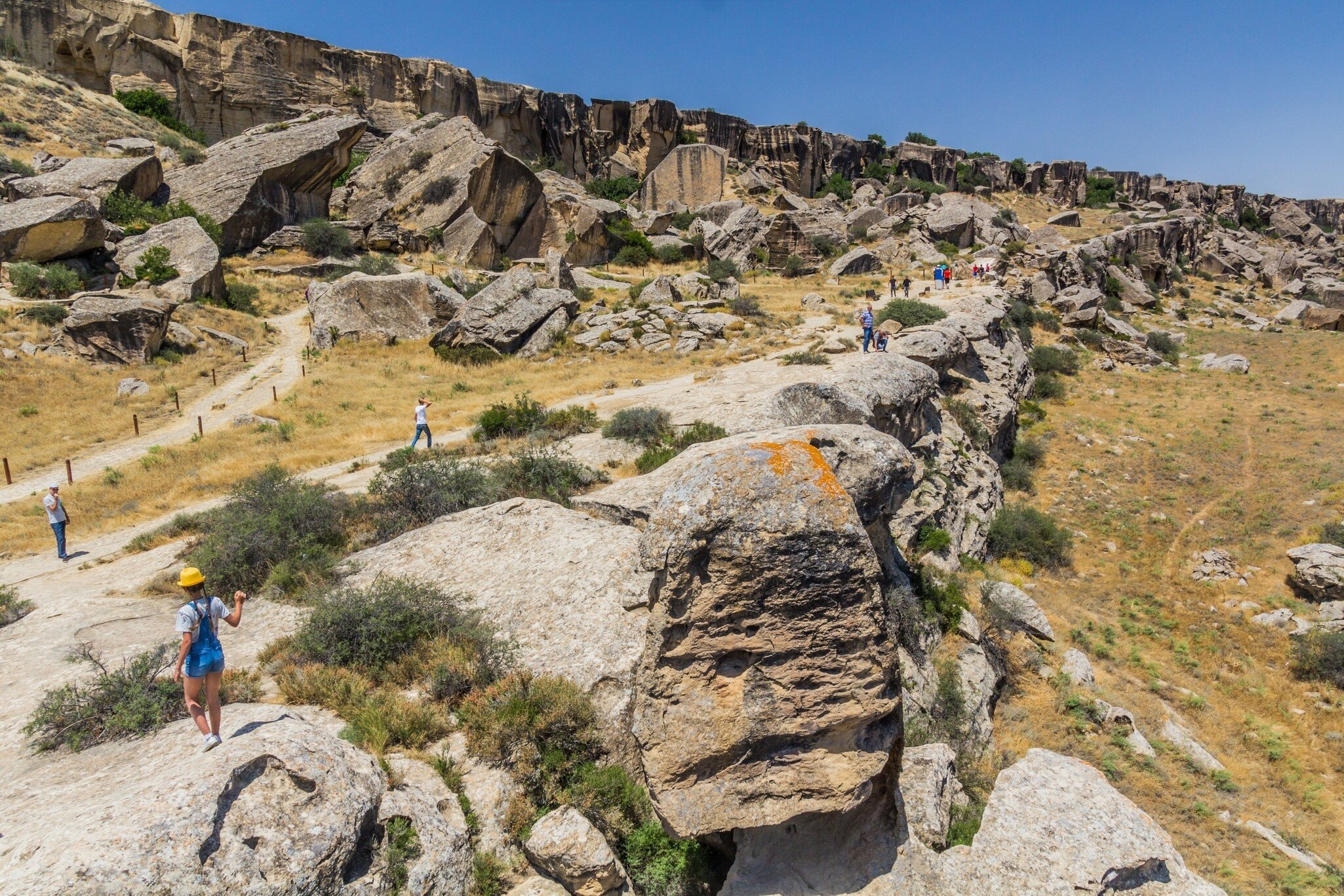  Tourists visit Gobustan petroglyph reserve, Azerbaijan. Overhead rock formations and blue sky.